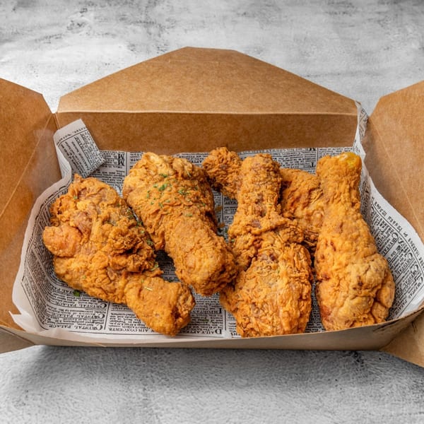 Crispy DAK Korean Fried Chicken pieces, seasoned with herbs, served in a brown takeout box.