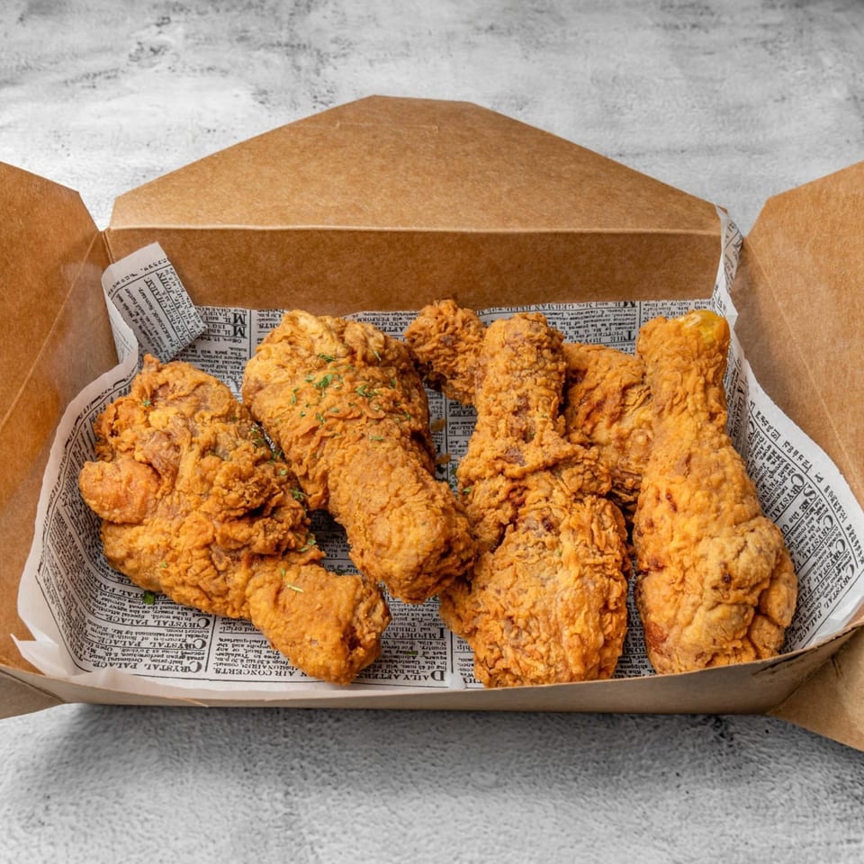 Crispy DAK Korean Fried Chicken pieces in a brown cardboard box lined with newspaper.