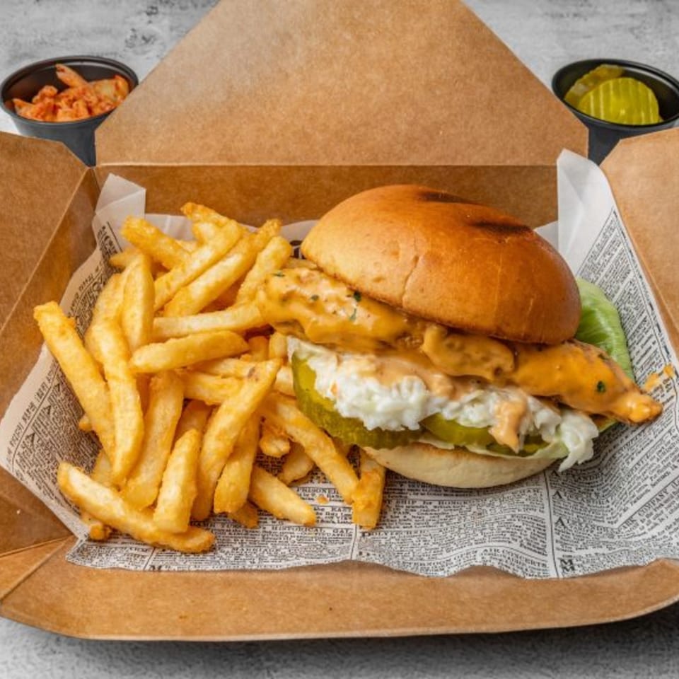 DAK Korean Fried Chicken sandwich with fries, kimchi, and pickles in a takeout box.