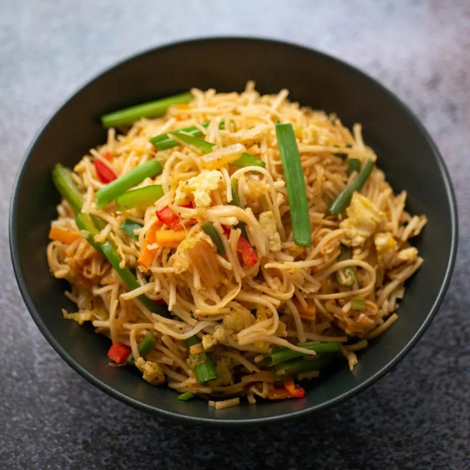 A close-up of a black bowl filled with Korean fried noodles, vegetables, and egg.