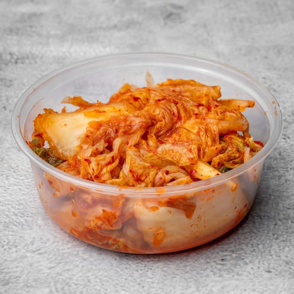 A clear plastic container filled with vibrant red kimchi, showcasing the fermented cabbage.