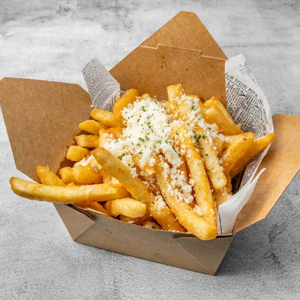Golden french fries topped with crumbled feta cheese and parsley in a brown paper container.