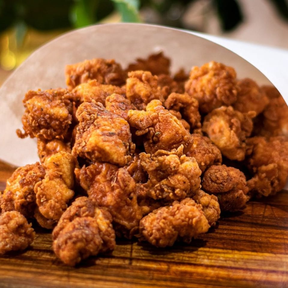 Crispy, golden-brown Korean fried chicken bites served in a paper cone on a wooden board.