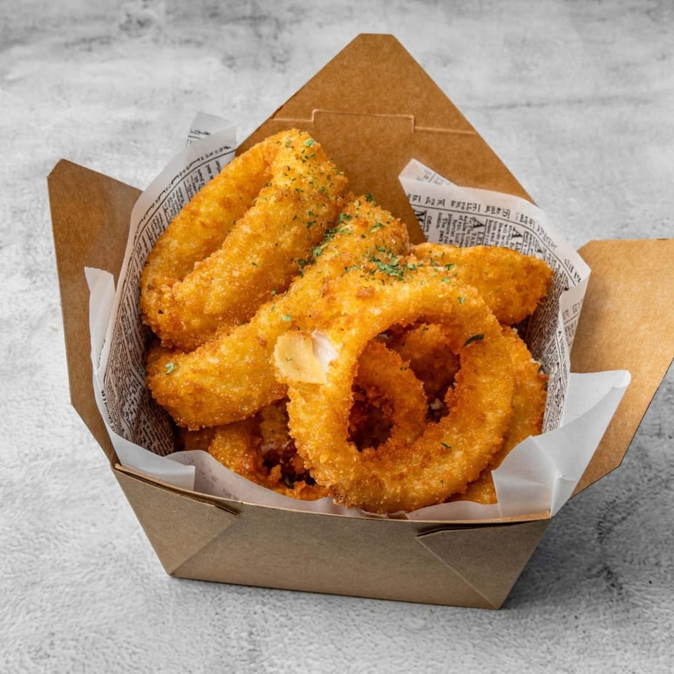 Crispy golden-brown onion rings, lightly seasoned with herbs, served in a brown paper box.