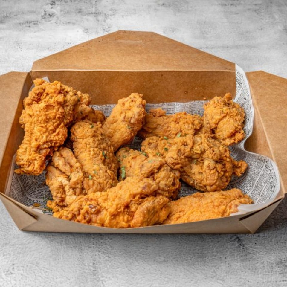 Crispy golden Korean fried chicken pieces in a brown takeout box lined with newspaper.