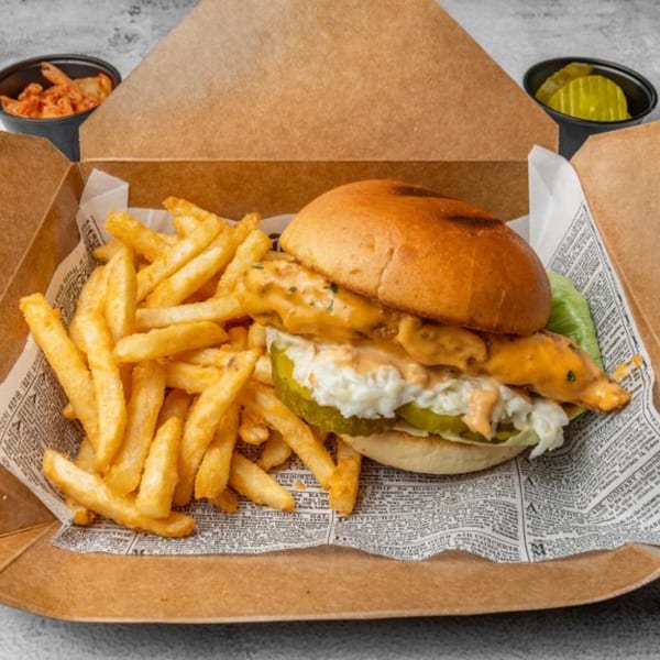 DAK Korean Fried Chicken sandwich with fries, kimchi, and pickles in a takeout box.